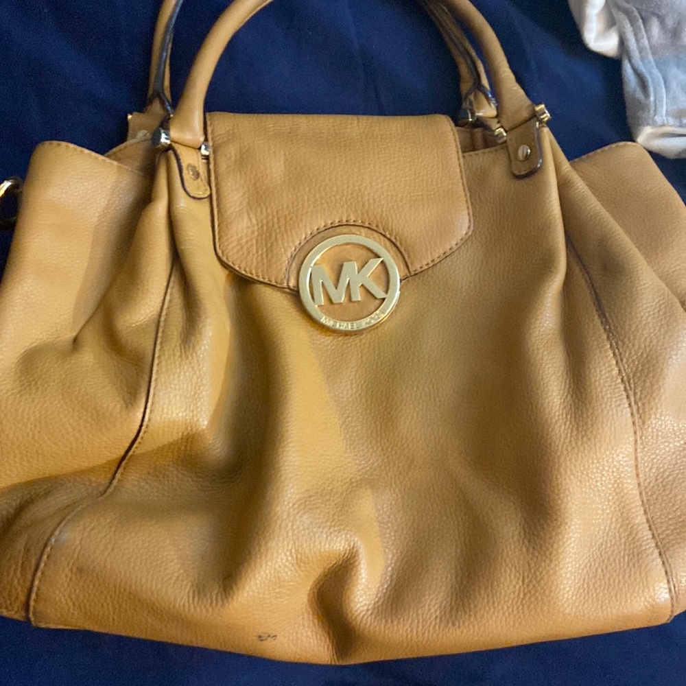Brown or tan MK purse with gold emblem and has hooks for a longer strap